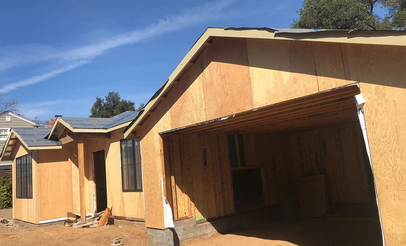 House under construction; exposed wood siding, open garage, blue sky.