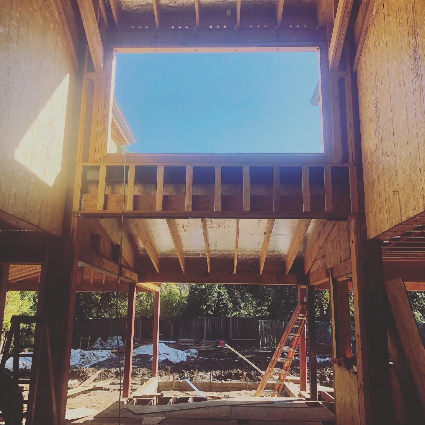 Interior view of a building under construction, showing wooden framing against a blue sky.