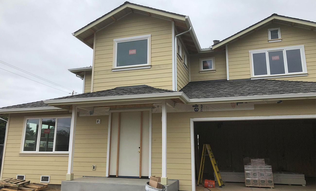 Two-story house under construction with yellow siding, gray roof, and open garage.