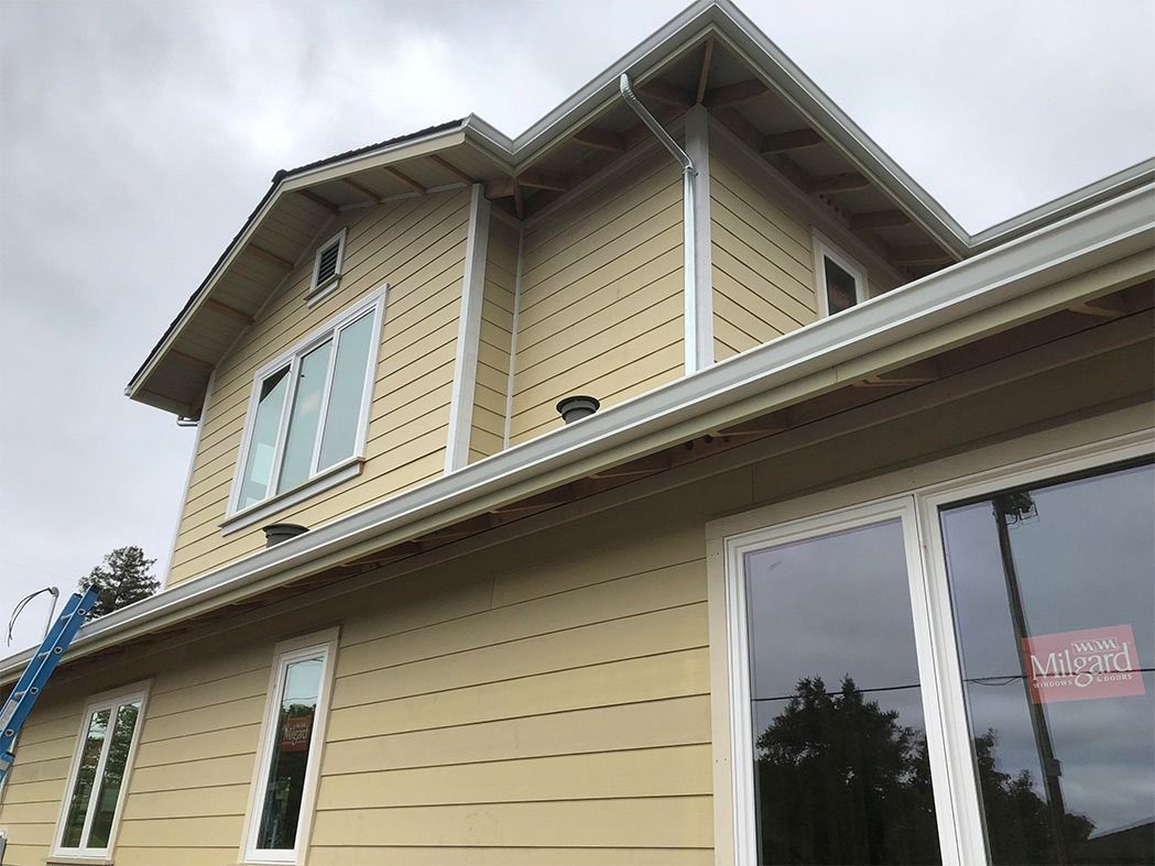 Beige siding on a two-story house with white-framed windows, under a cloudy sky.