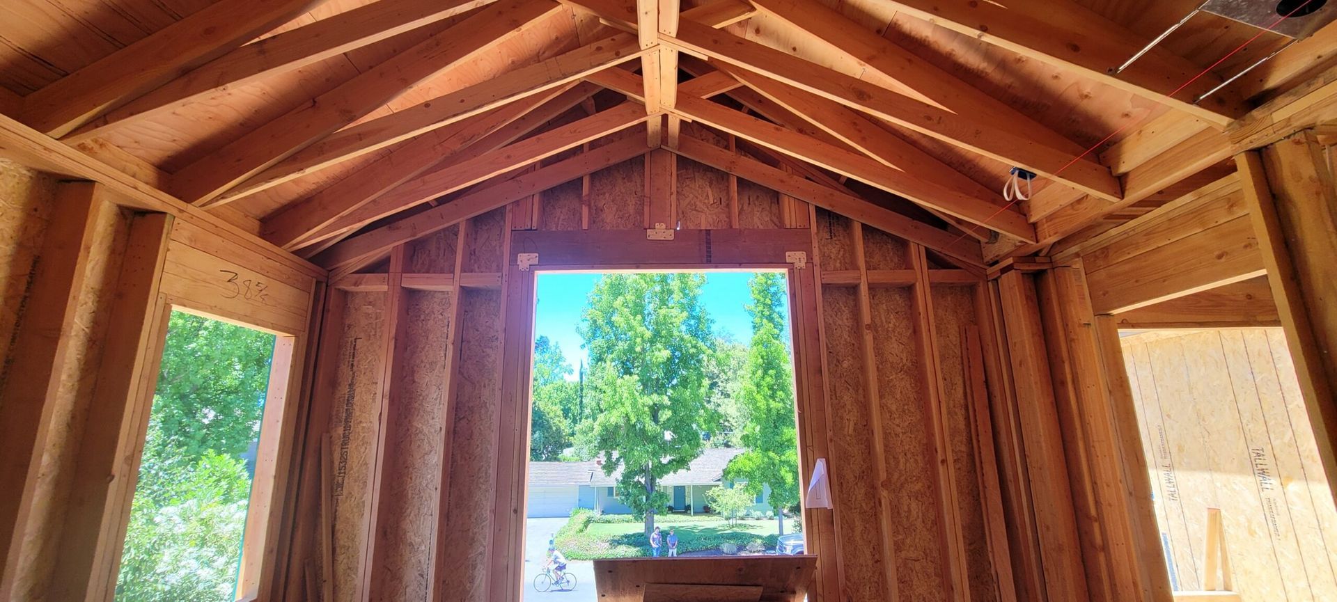 Interior view of a wooden structure in progress, with a view of trees through an opening.