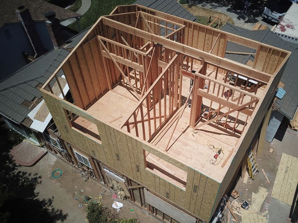 Two-story house under construction; wooden frame, exterior walls, roof partially complete, clear sky.