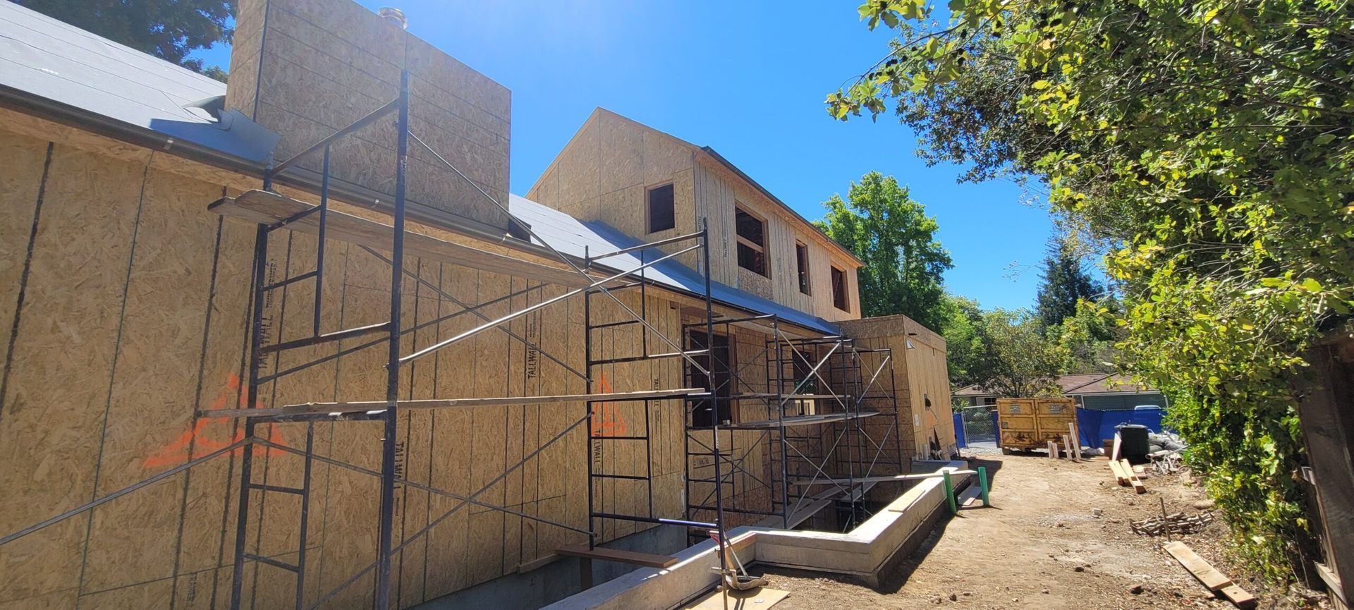 A house under construction with scaffolding and exposed wooden siding on a sunny day.