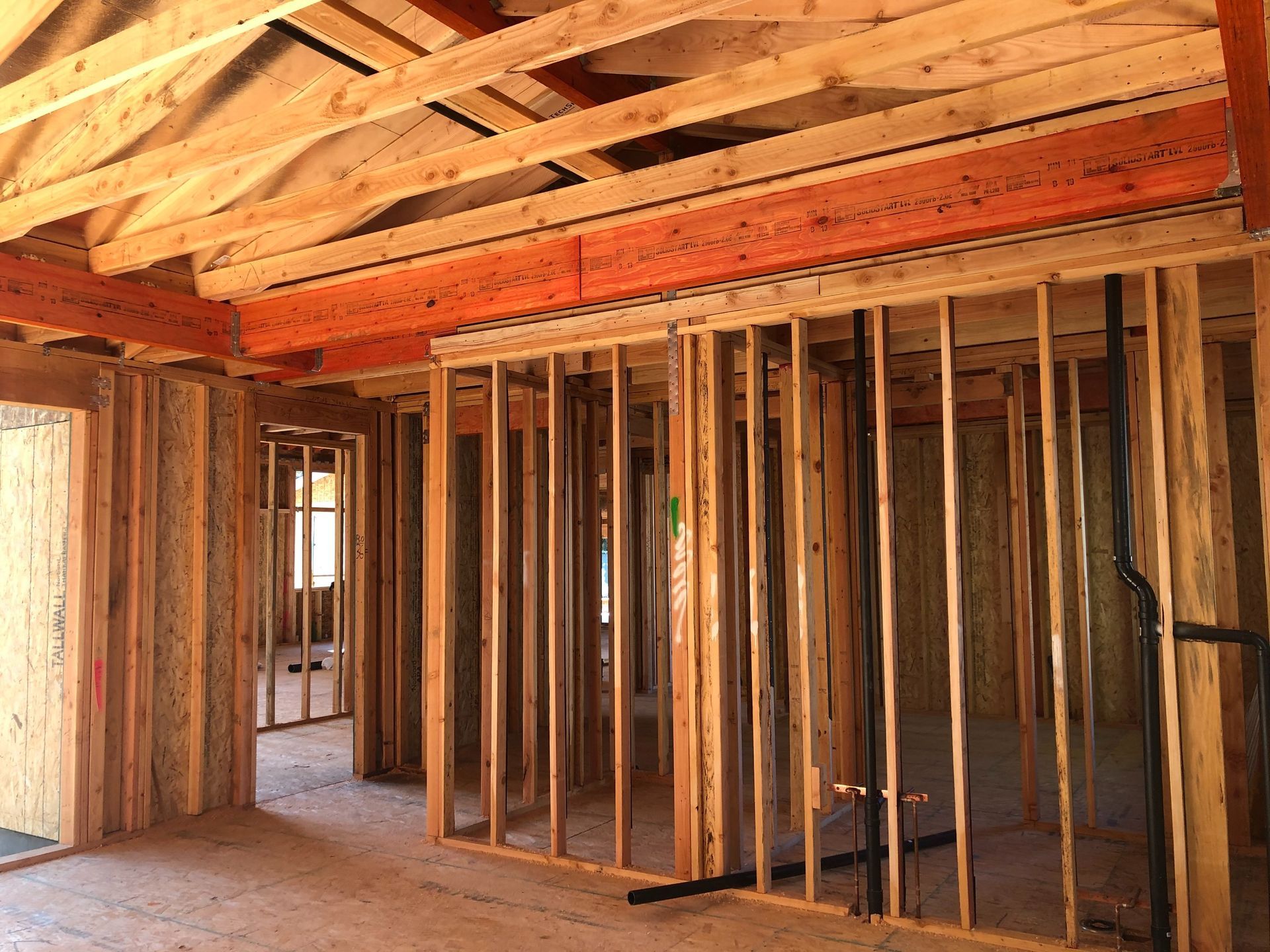 Interior of a house under construction; wooden studs, beams, and framing visible.
