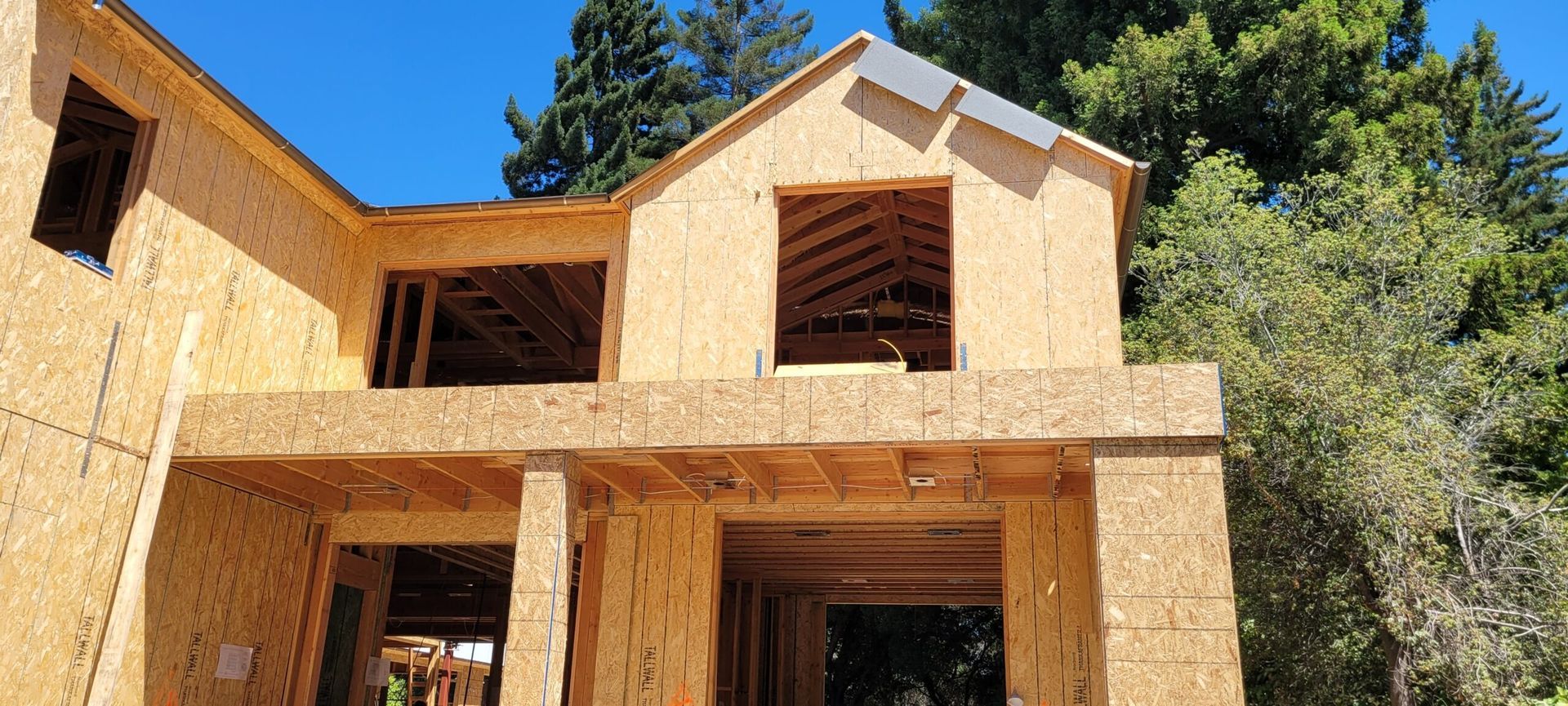 Wood-framed house under construction; blue sky, green trees in background.