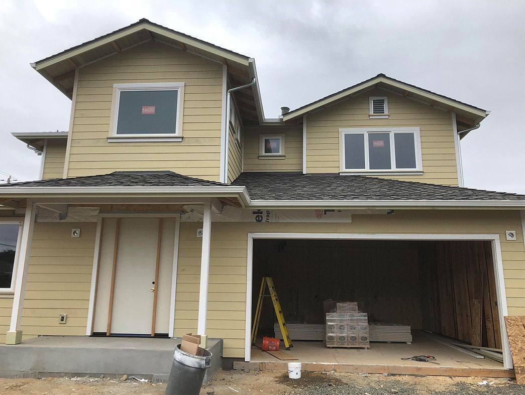 Two-story house under construction with yellow siding, gray roof, and open garage.