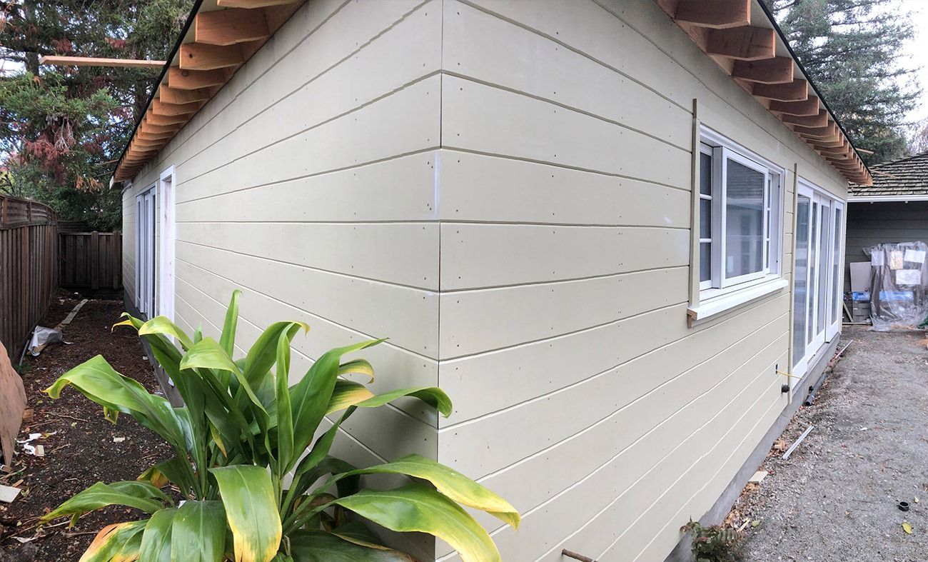 Light green building exterior with horizontal siding, two windows, and a plant.