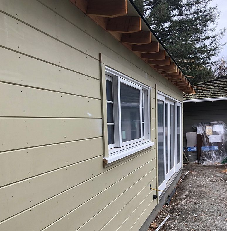 Exterior of a light yellow building with white-framed windows and a wooden roof overhang.