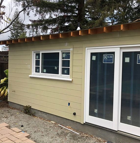 Beige building with white-framed window and sliding glass doors. Brown wooden trim. Brick pathway.