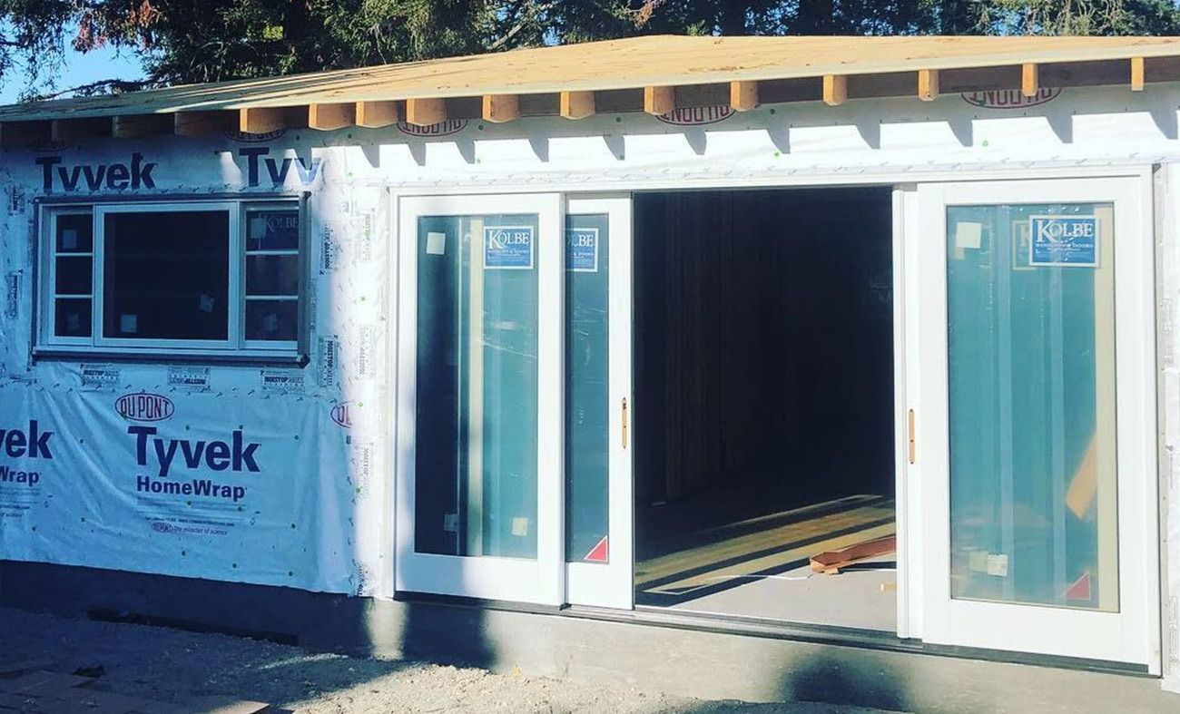 Building exterior under construction with Tyvek wrap, sliding doors, and window.