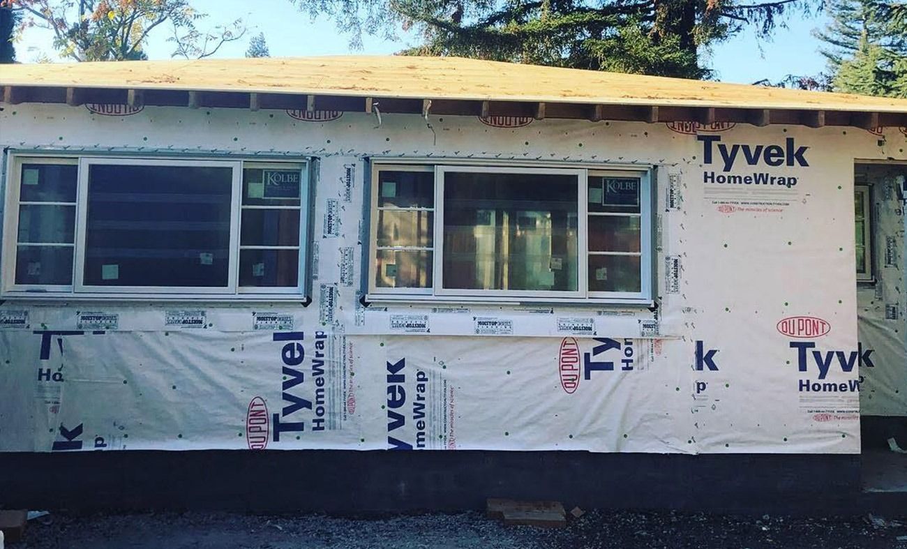 Exterior view of a house under construction; windows installed, covered in Tyvek, and plywood roof.
