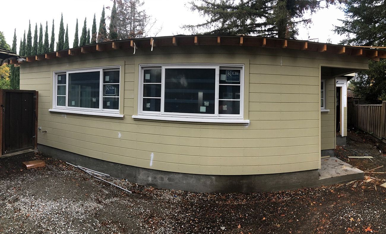 Beige building with white-framed windows, under construction, with a curved wall section.