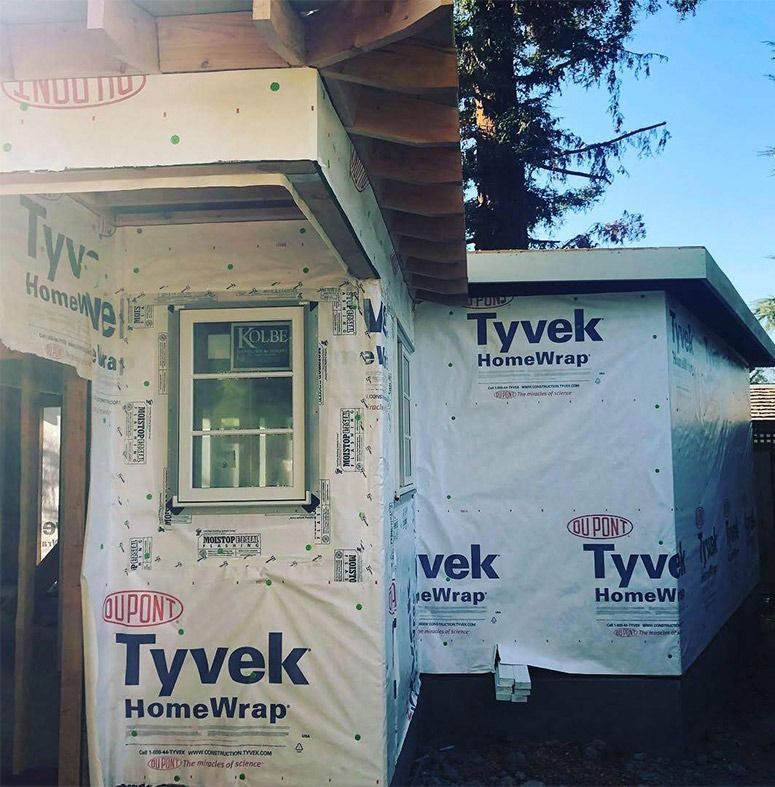 Building exterior wrapped in white Tyvek HomeWrap, window visible.