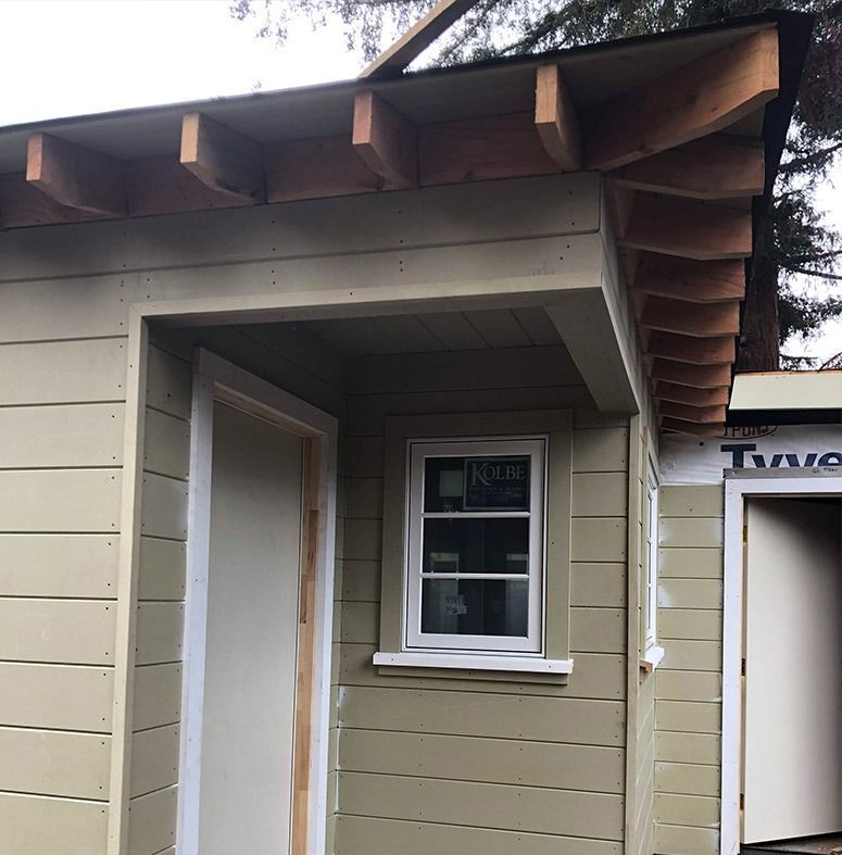 Exterior of a building under construction, featuring a doorway, window, and exposed roof beams.