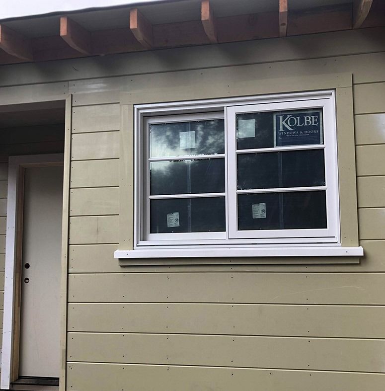 Exterior of a tan building with a white-framed sliding window and a door.
