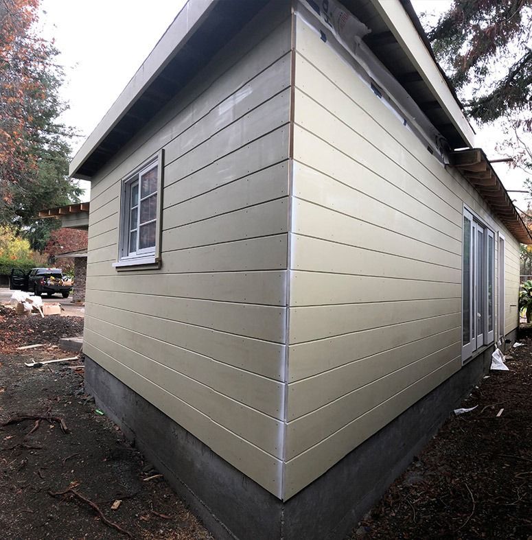 Tan siding installed on a newly constructed building. Window, doors, and corner trim visible.