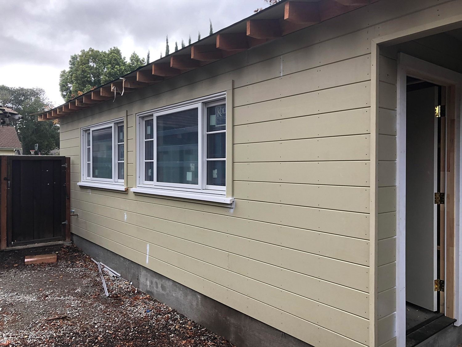 Tan-sided building with white-framed windows, open door, and exposed roof supports.