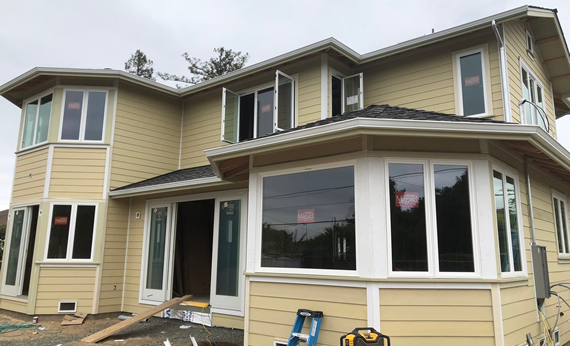 Two-story house with yellow siding, white trim, and newly installed windows; construction in progress.