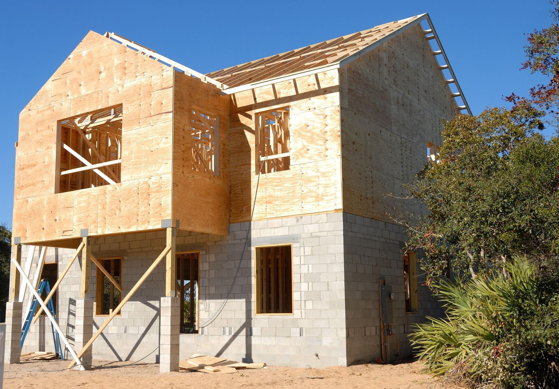 Two-story house under construction: cinder block base, wooden frame, plywood siding.