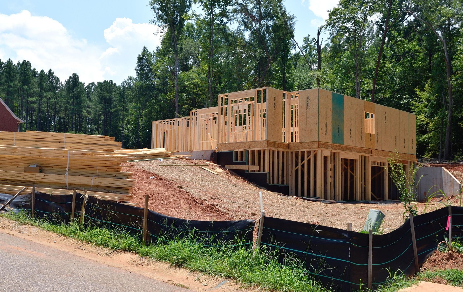 Construction site with a partially framed house, lumber, and erosion control.