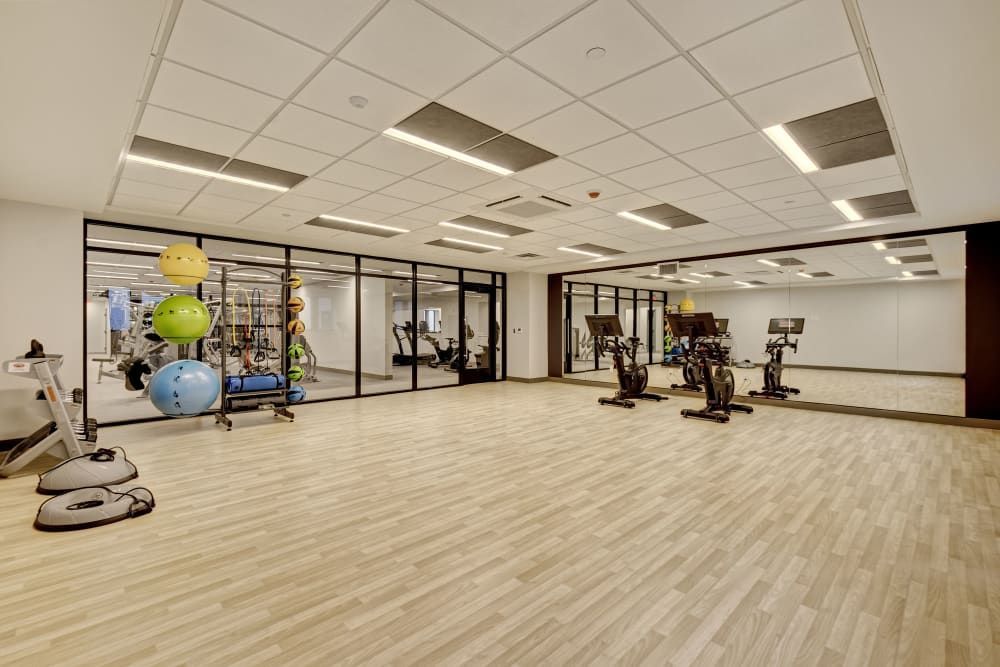 A modern gym with exercise equipment like stationary bikes, medicine balls, and weights, along with a large mirror and glass walls.