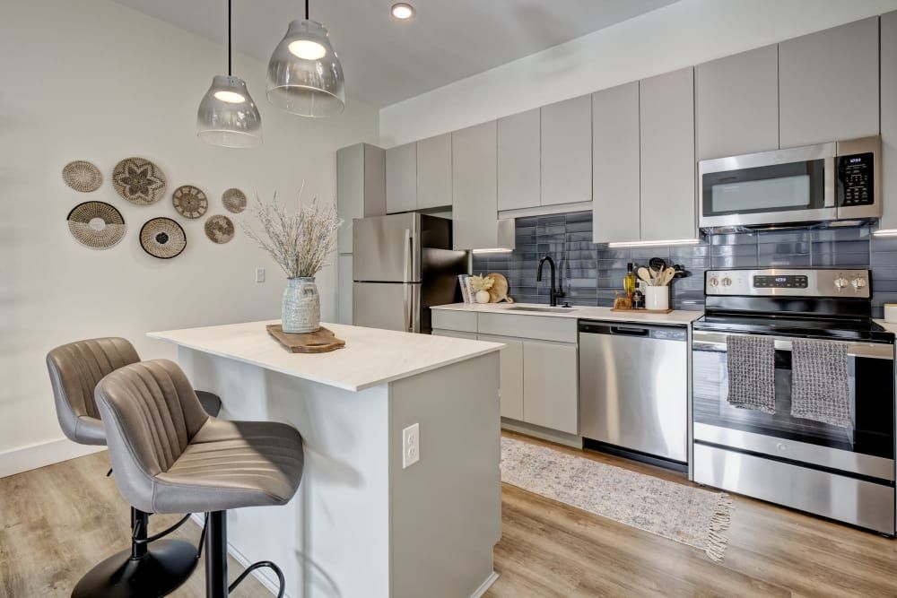 A kitchen with stainless steel appliances , a refrigerator , a microwave , and a bar.