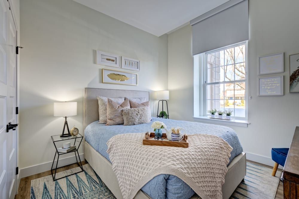 A bedroom with a bed , nightstand , lamp and window.