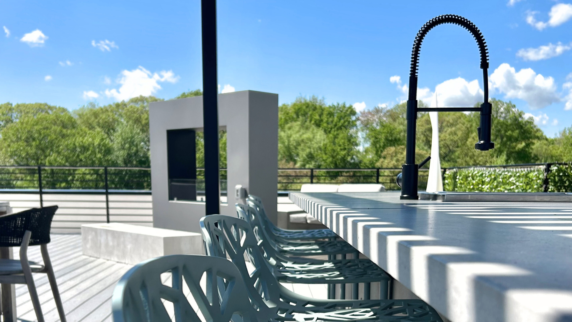 Modern rooftop lounge seating bar with a fireplace.  Lush green tree line and blue cloudy sky