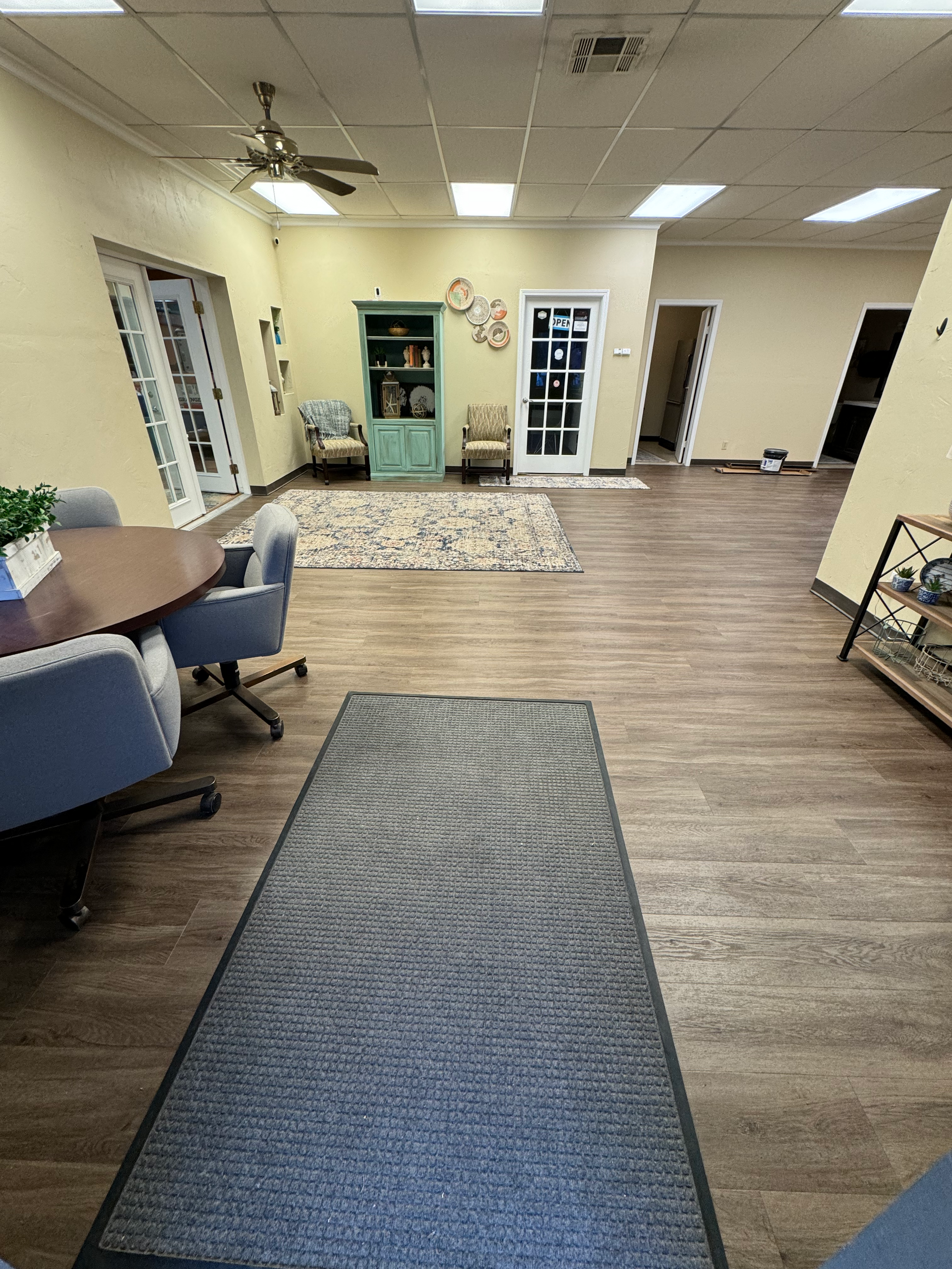 a large room with a table , chairs , a rug and a ceiling fan .