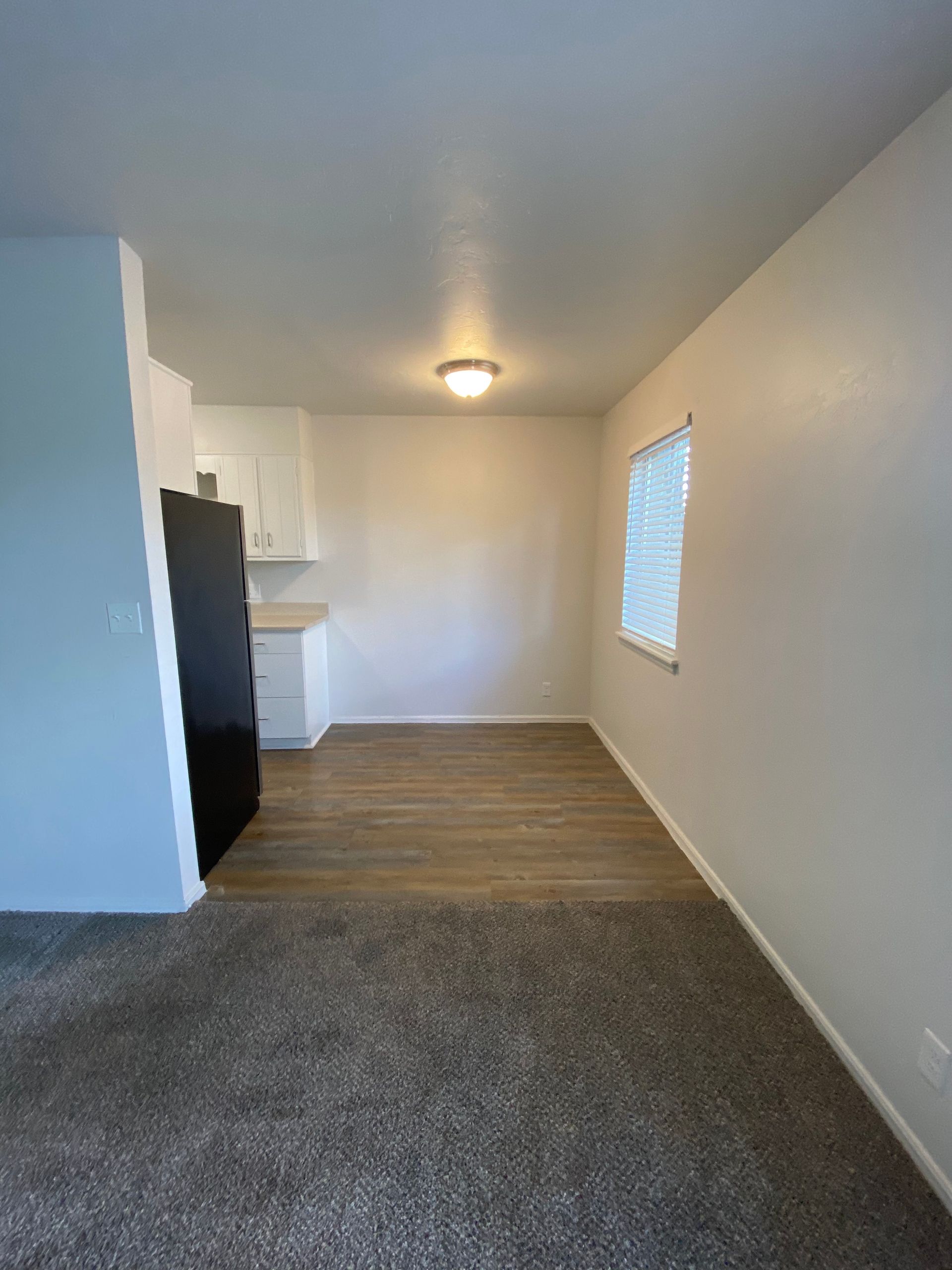 an empty living room with a black refrigerator and a window .