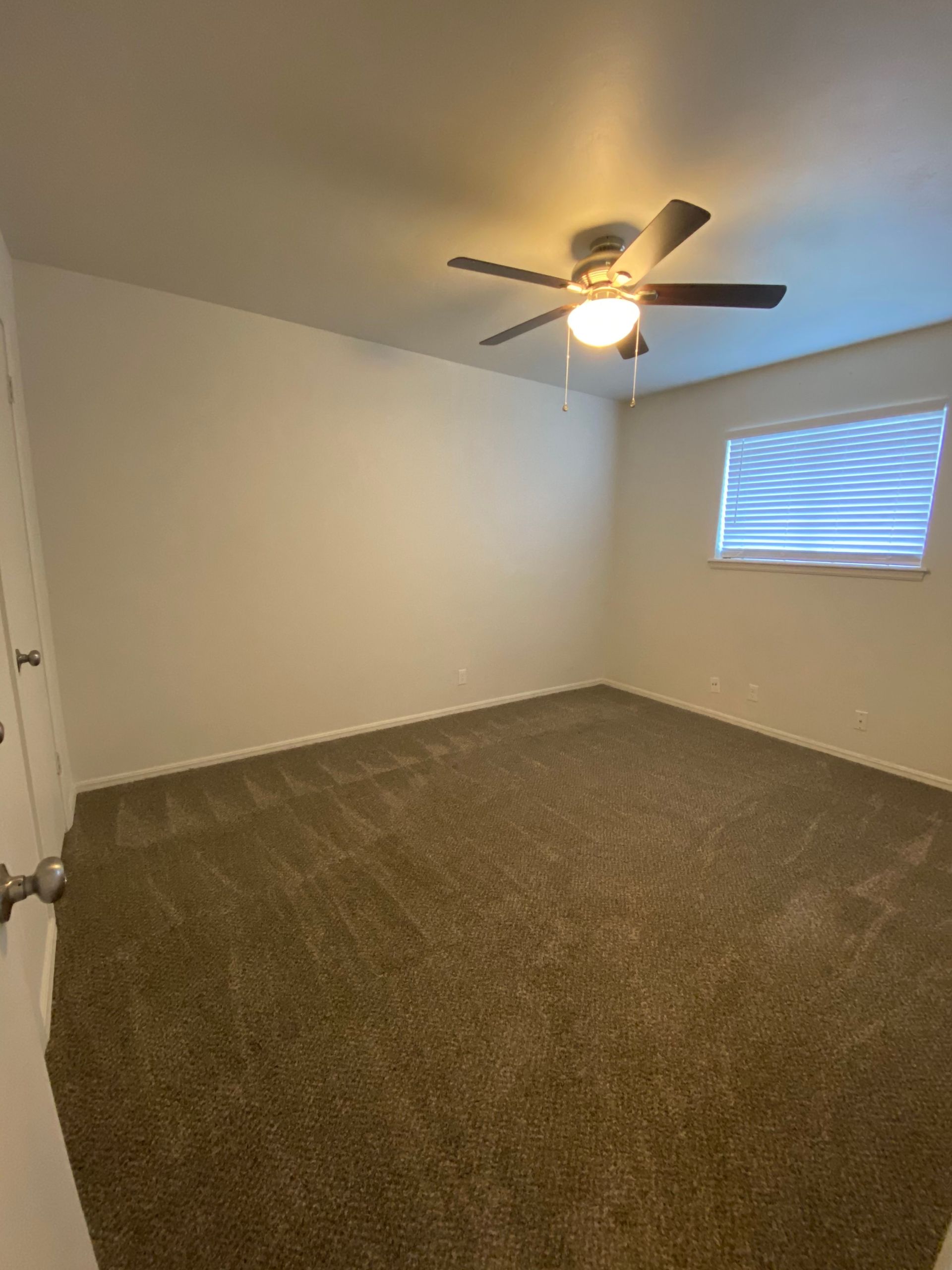 an empty bedroom with a ceiling fan and a window .