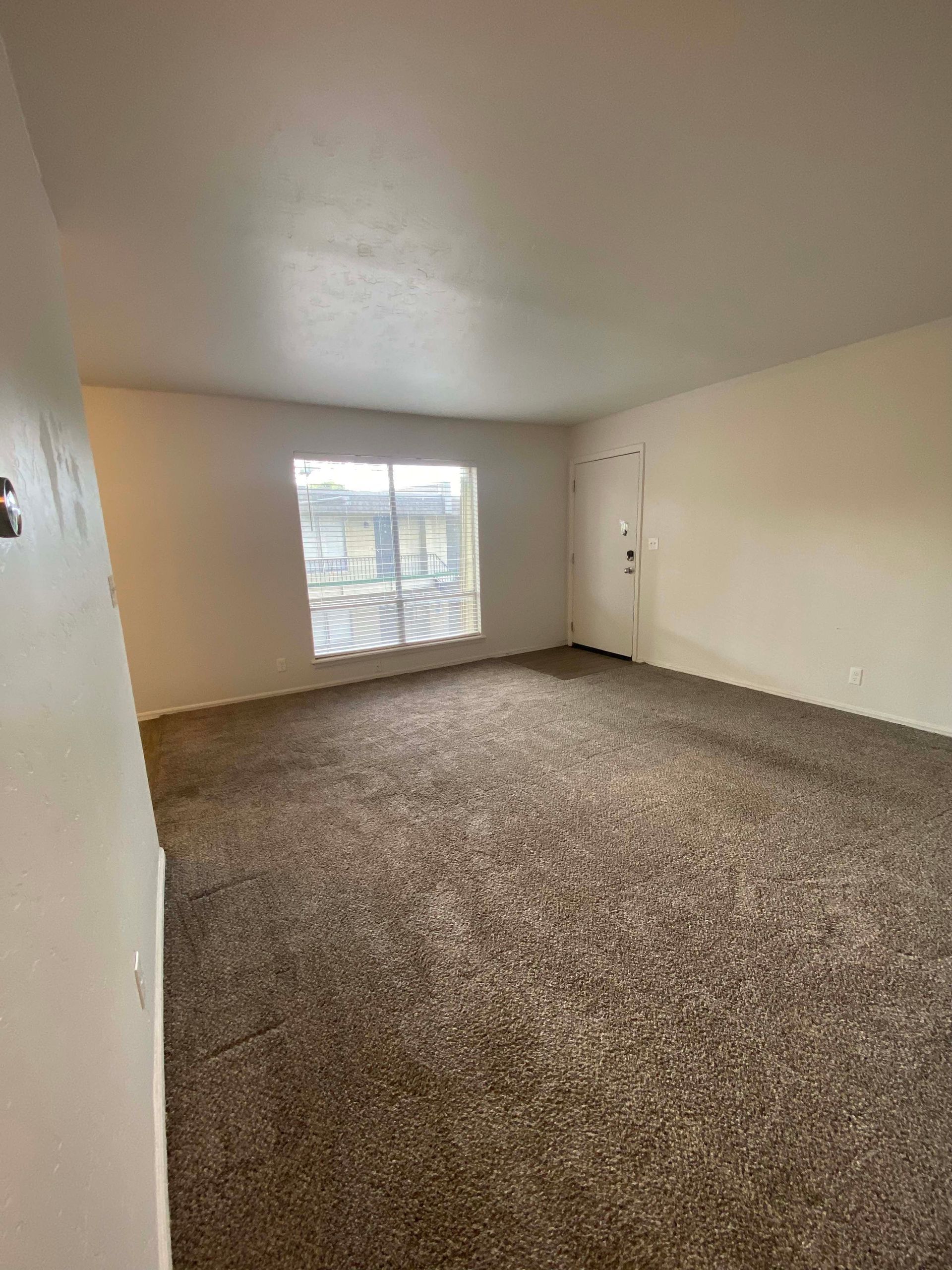 an empty living room with a large window and a brown carpet .