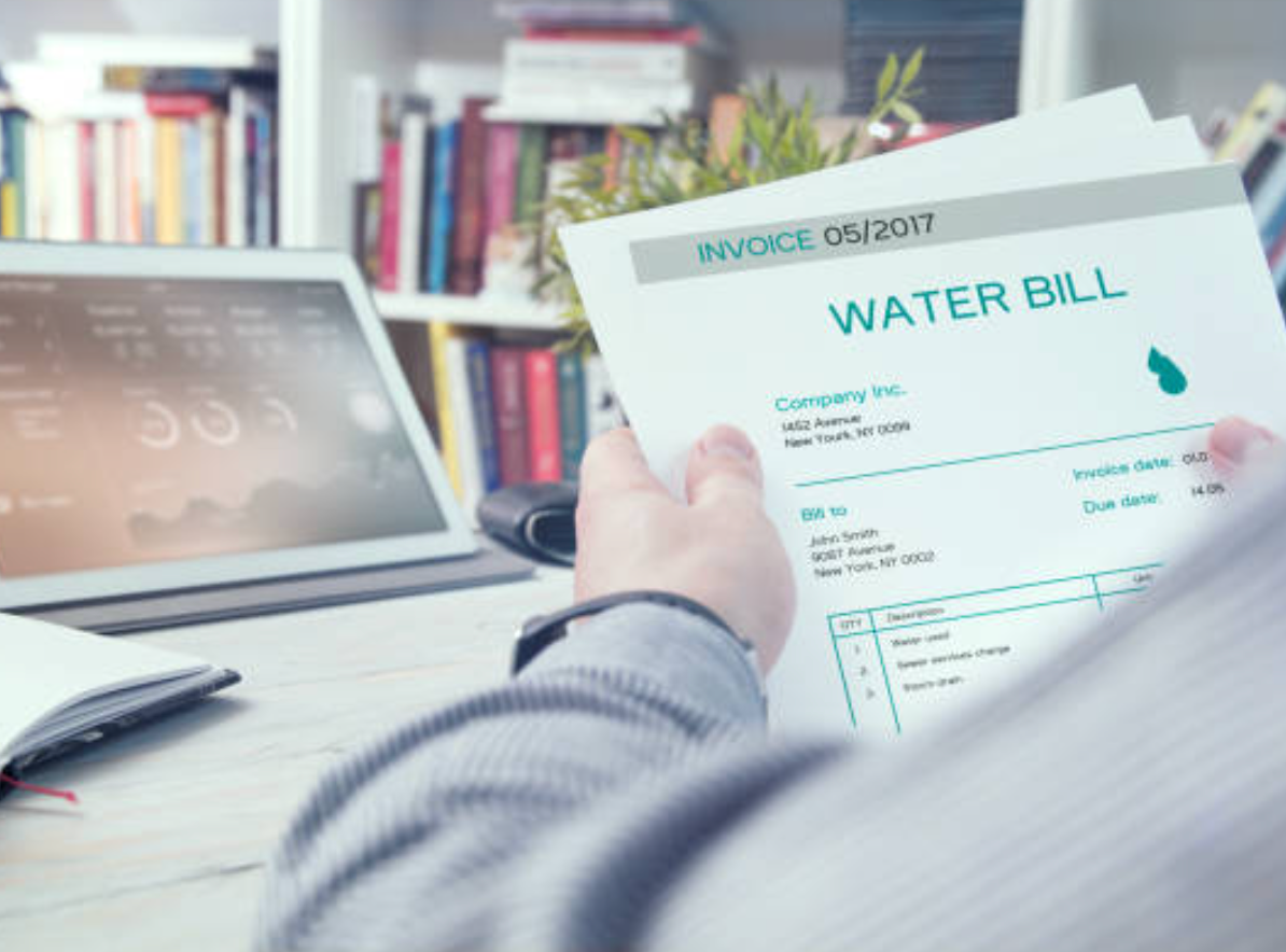 A Person is Holding a Water Bill in Front of a Laptop — Absolute Plumbing Australia in Darwin, NT