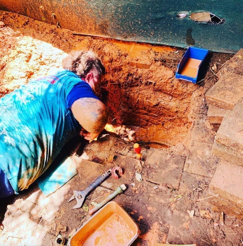 A Man in a Blue Shirt is Digging in the Dirt — Absolute Plumbing Australia in Darwin, NT