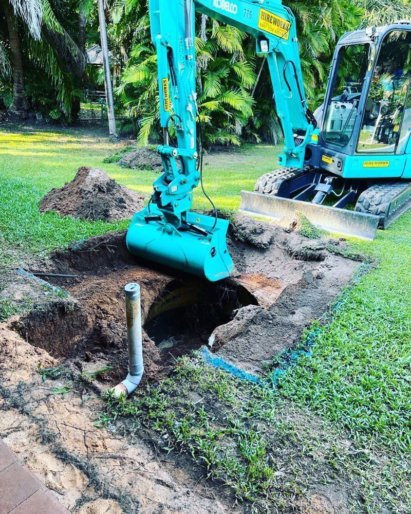 A Blue Excavator is Digging a Hole in the Ground — Absolute Plumbing Australia in Darwin, NT