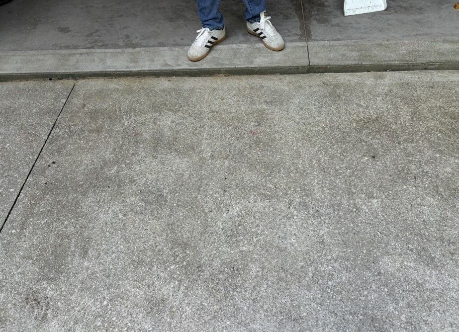 A person wearing white adidas shoes is standing on a concrete surface