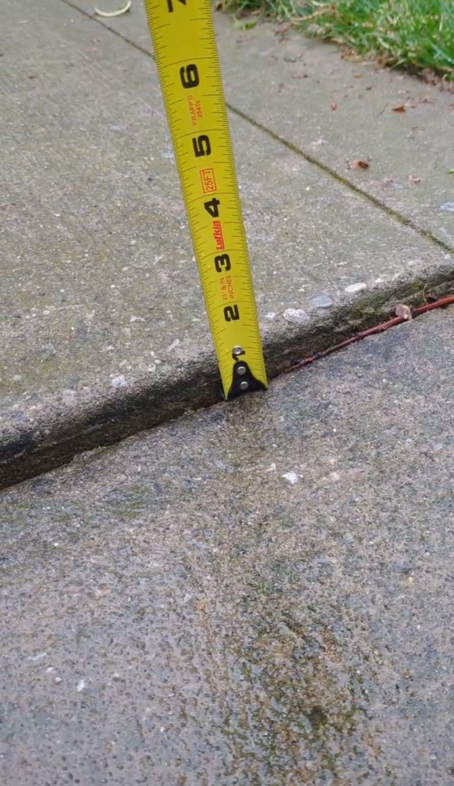 A yellow tape measure is measuring a concrete sidewalk.