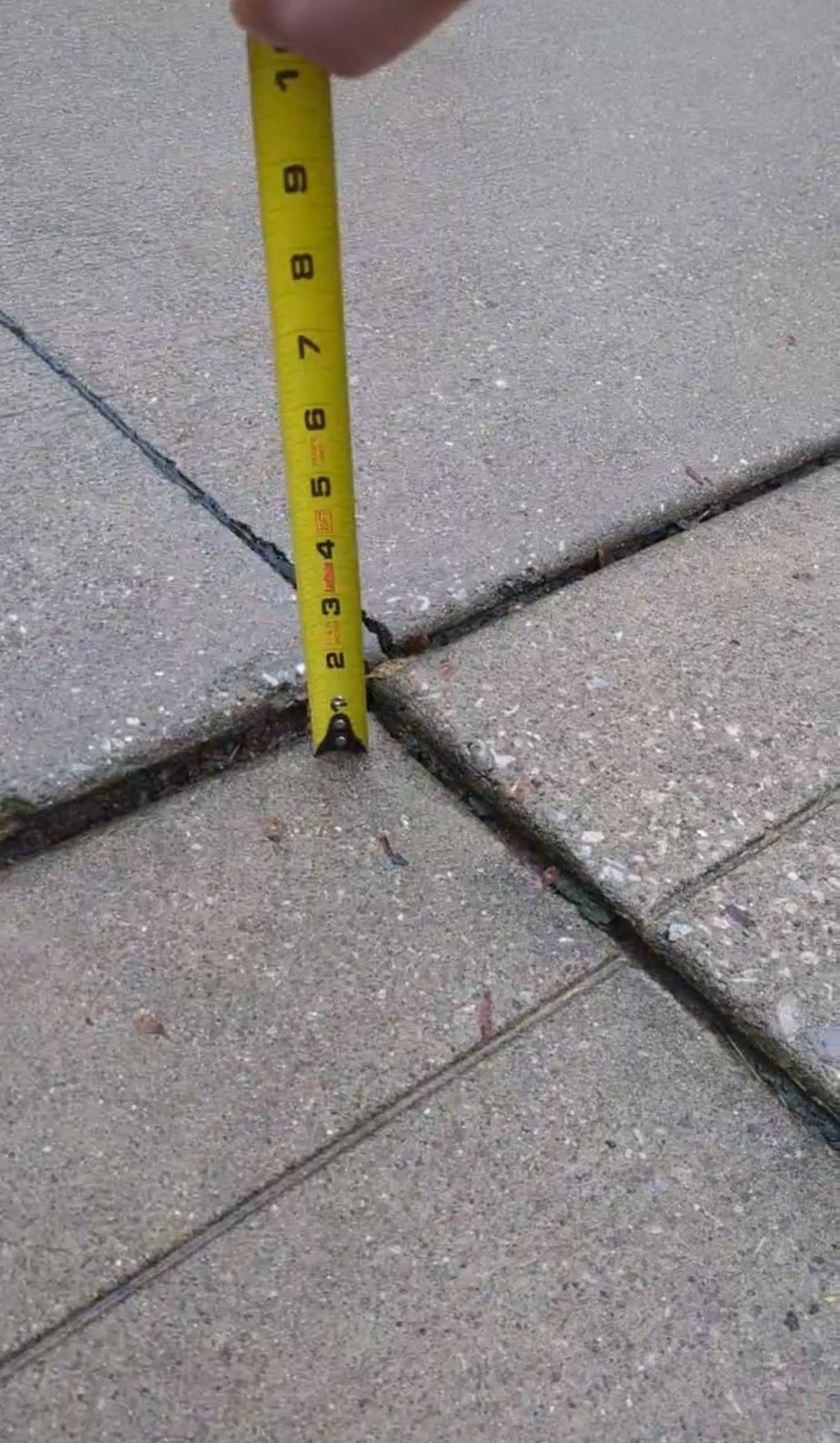 A person using a measuring tape on a sidewalk, indicating a measurement process in progress.