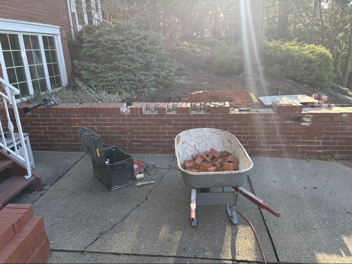 A wheelbarrow filled with bricks is on a patio in front of a brick wall.