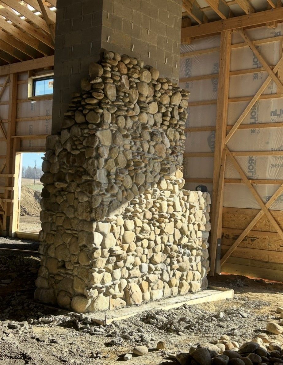 A large stone chimney is in the middle of a building under construction.