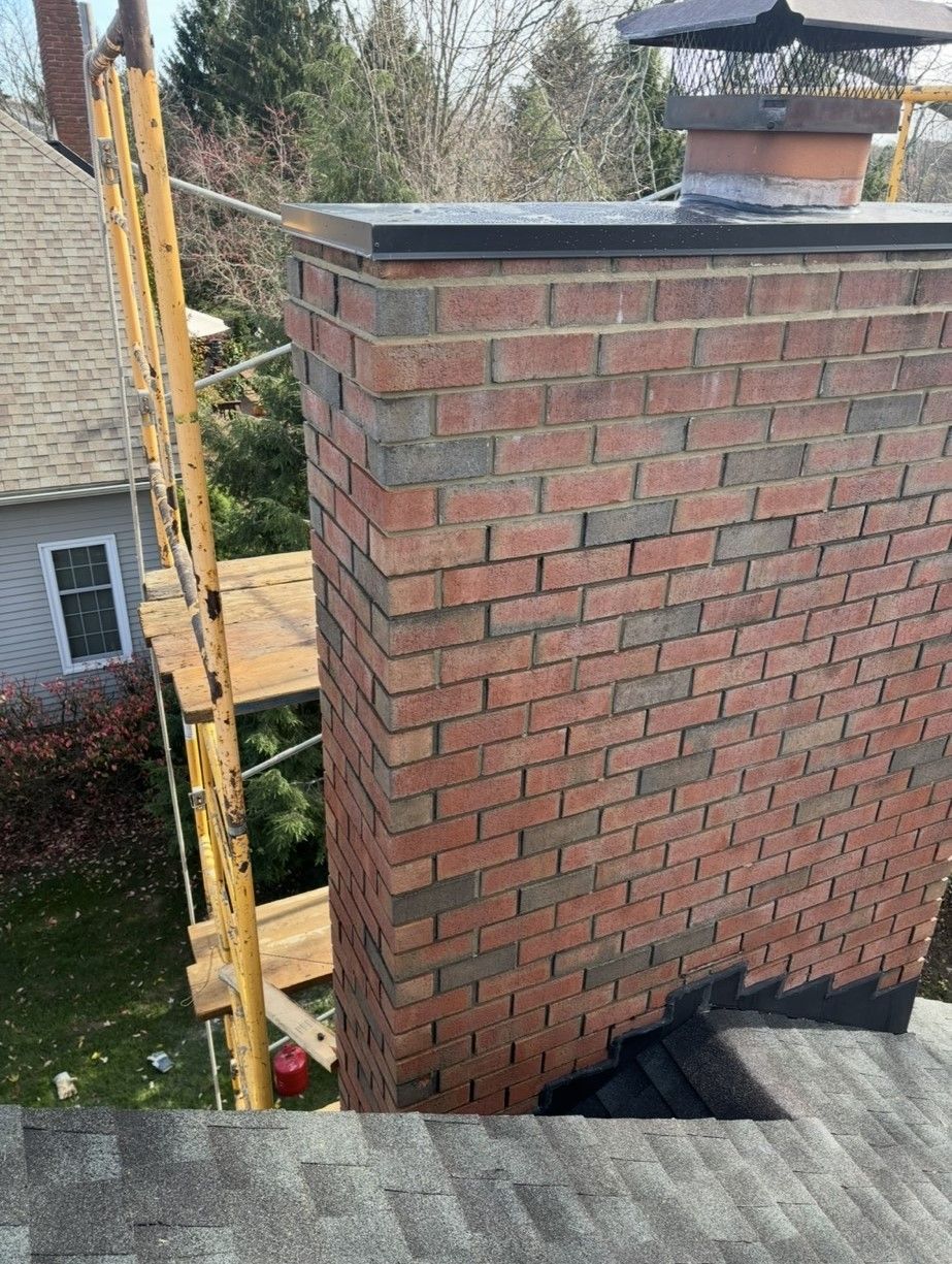 A brick chimney is being built on the roof of a house.