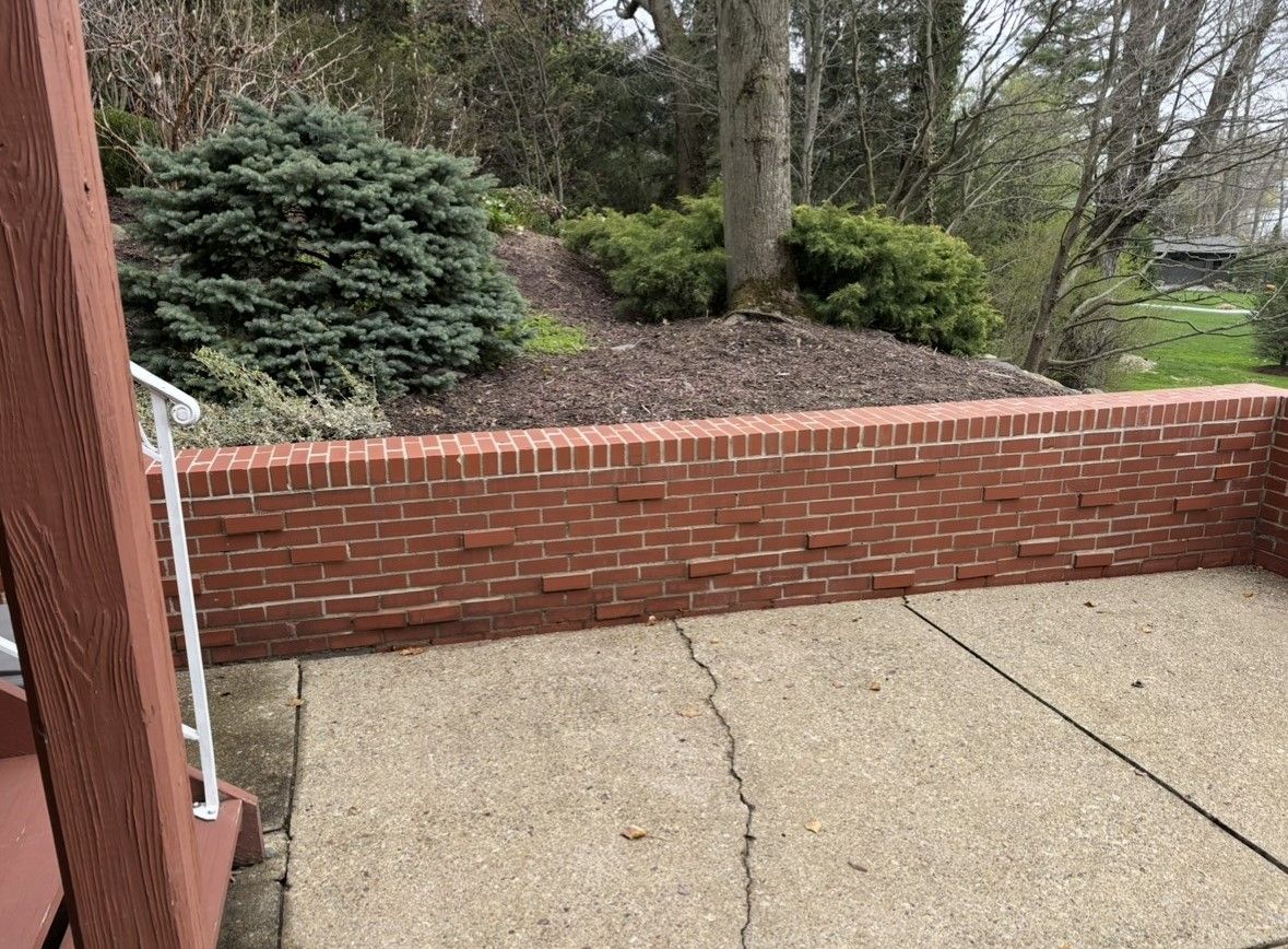 A brick wall surrounds a patio with trees in the background.