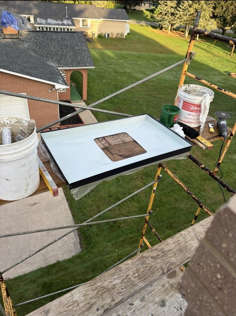 A metal tray with a square cutout sits on scaffolding, surrounded by a white bucket.