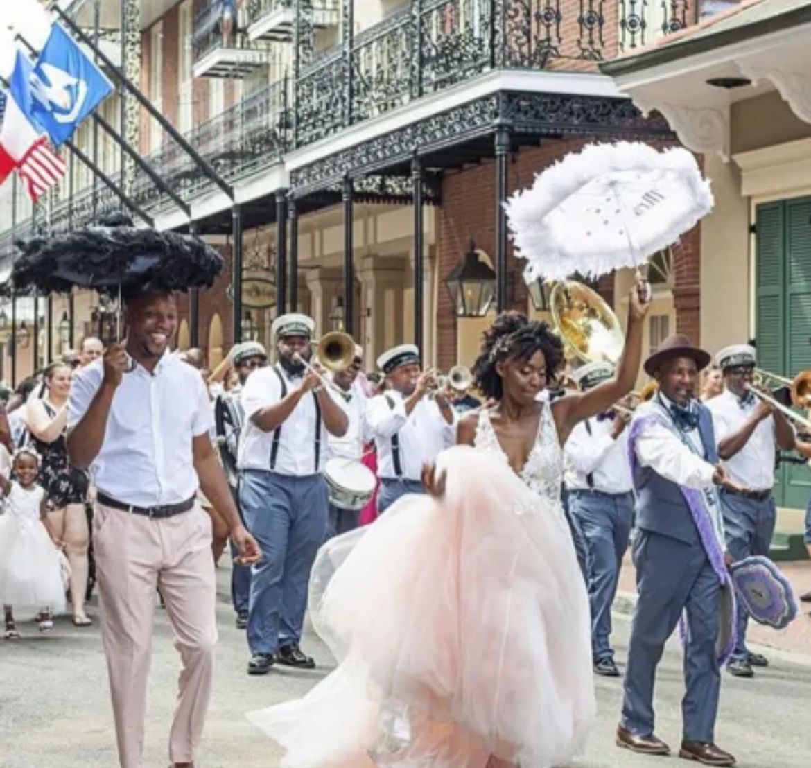 Wedding parade in New Orleans with a band. Bride in gown, couple with umbrellas lead the joyful march.