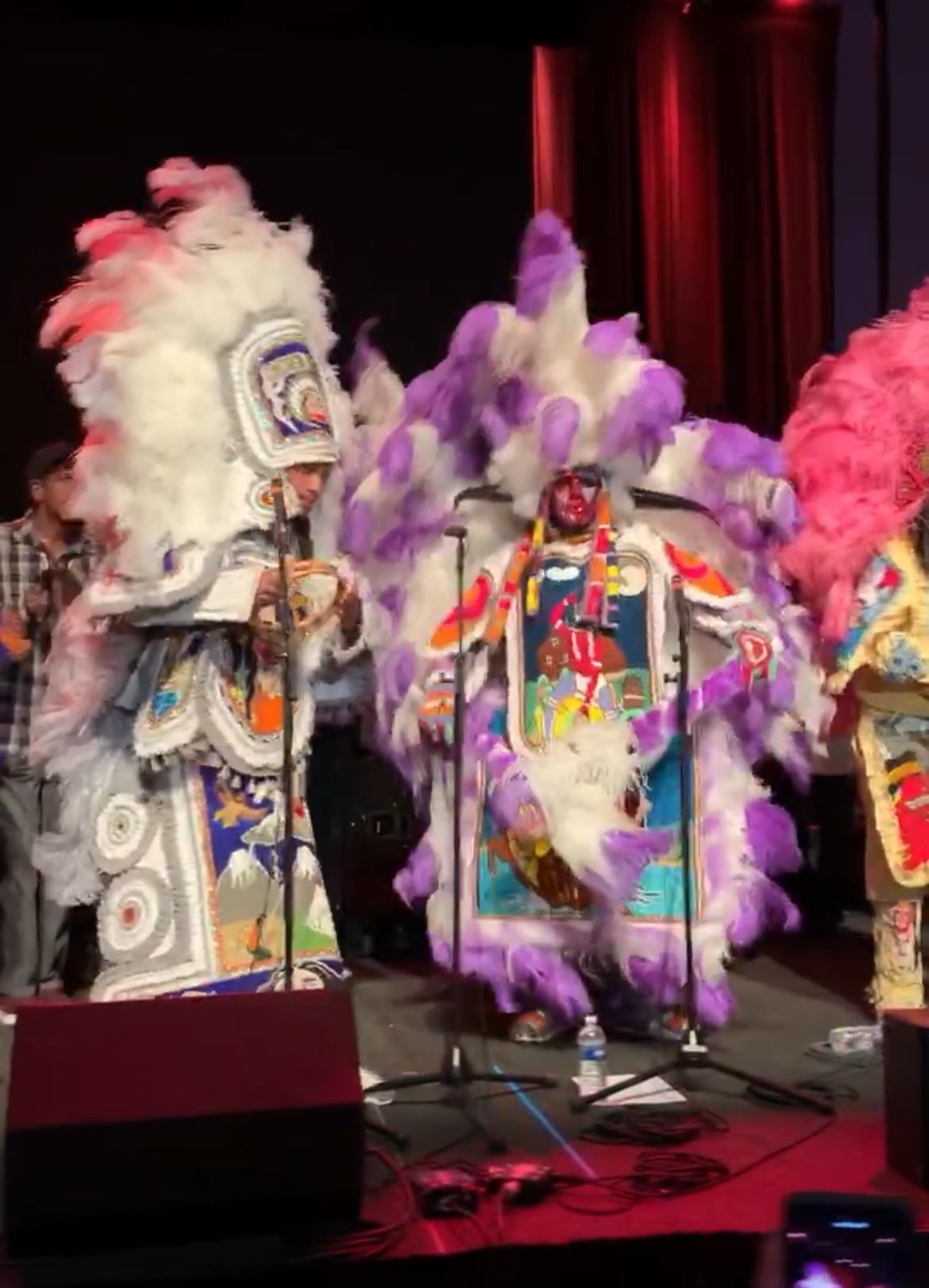 Two men in elaborate Mardi Gras Indian suits with feathers and beads on stage.