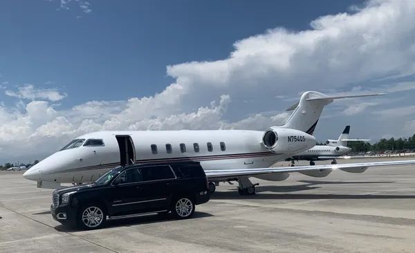 A car is parked next to a private jet on a runway.
