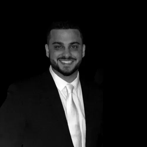 Ray Breslin in a suit and tie is smiling in a black and white photo .