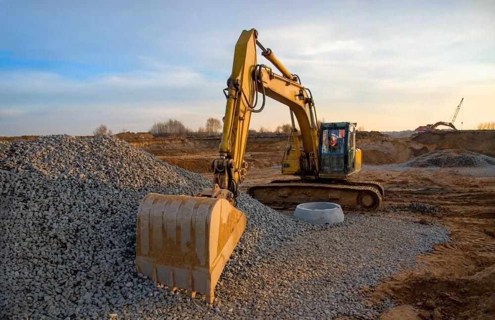 A yellow excavator is moving gravel on a construction site.