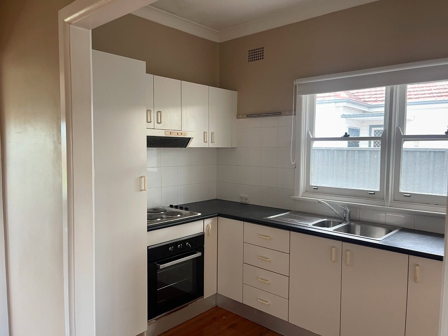 Small White Kitchen With Black Countertops, a Window, and Wood Flooring — Ecowave Solutions In Gosford, NSW