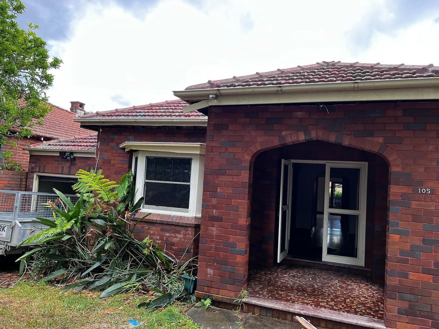 Red Brick House With an Open Doorway and Window, Overgrown Foliage — Ecowave Solutions In Gosford, NSW